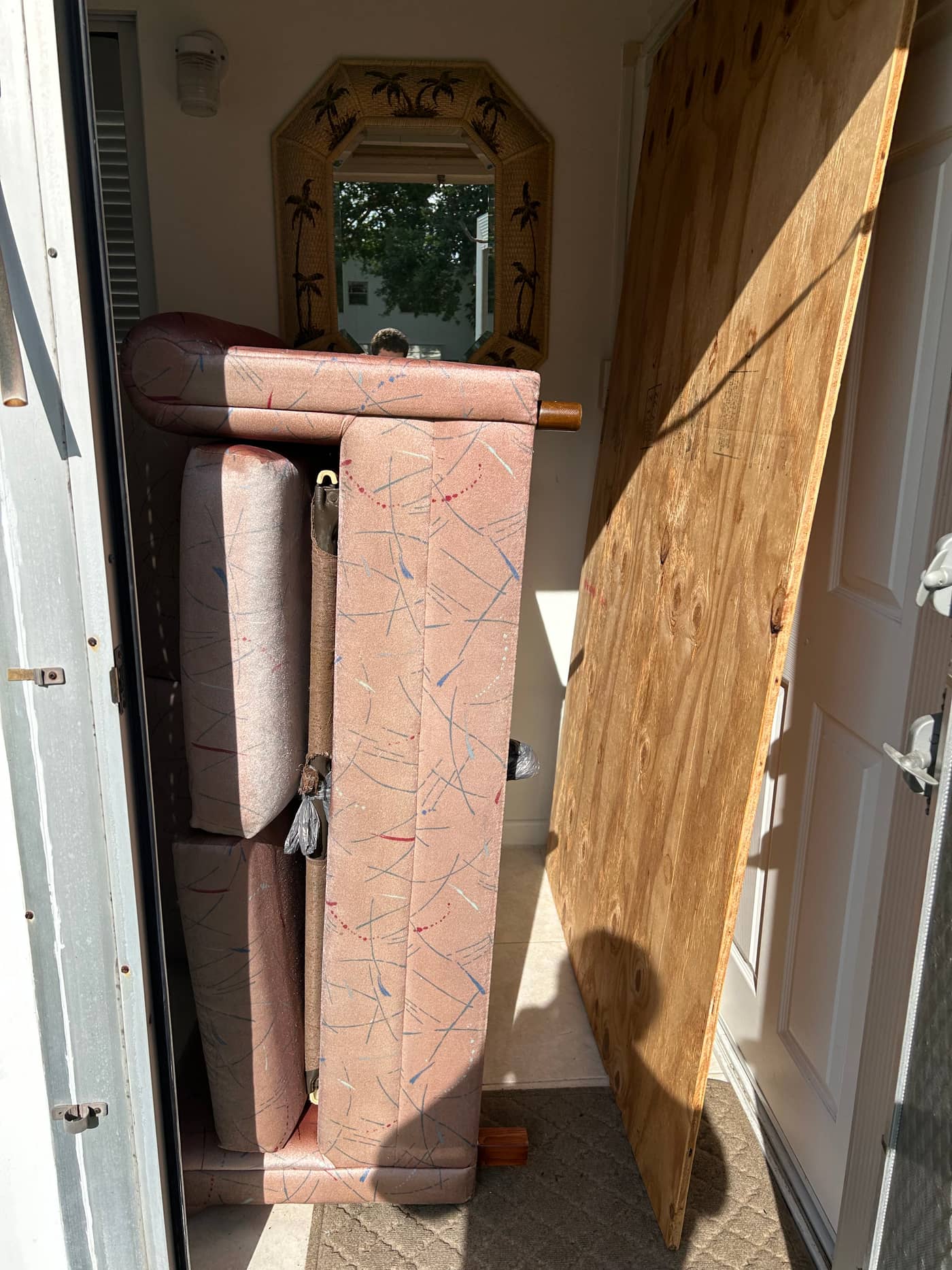 A pink upholstered sofa stood on end with its cushions, and a large sheet of plywood, wedged in a front doorway and blocking the entrance