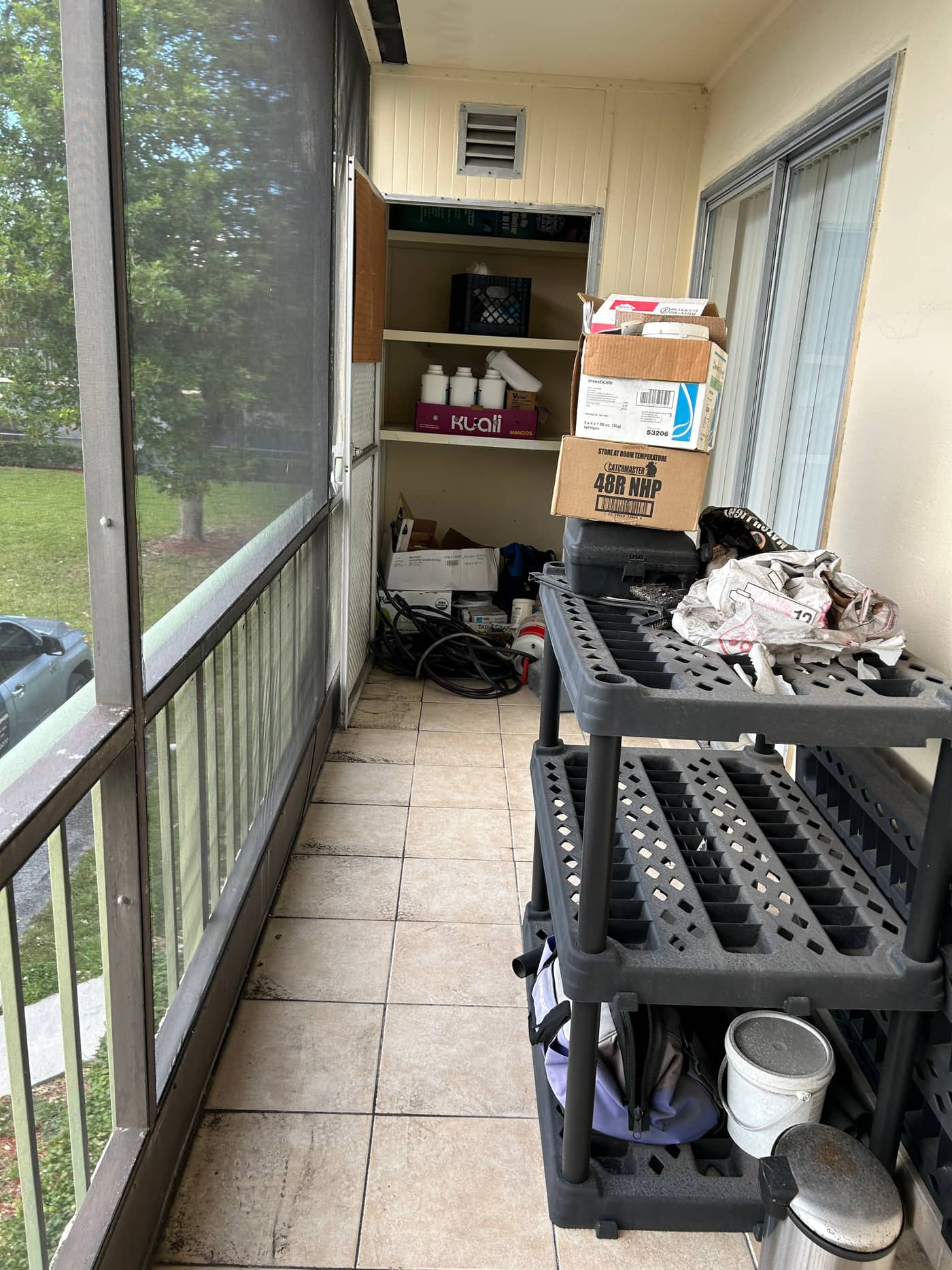 A screened patio with a plastic shelving unit, cardboard boxes, buckets and stored household items filling the walkway