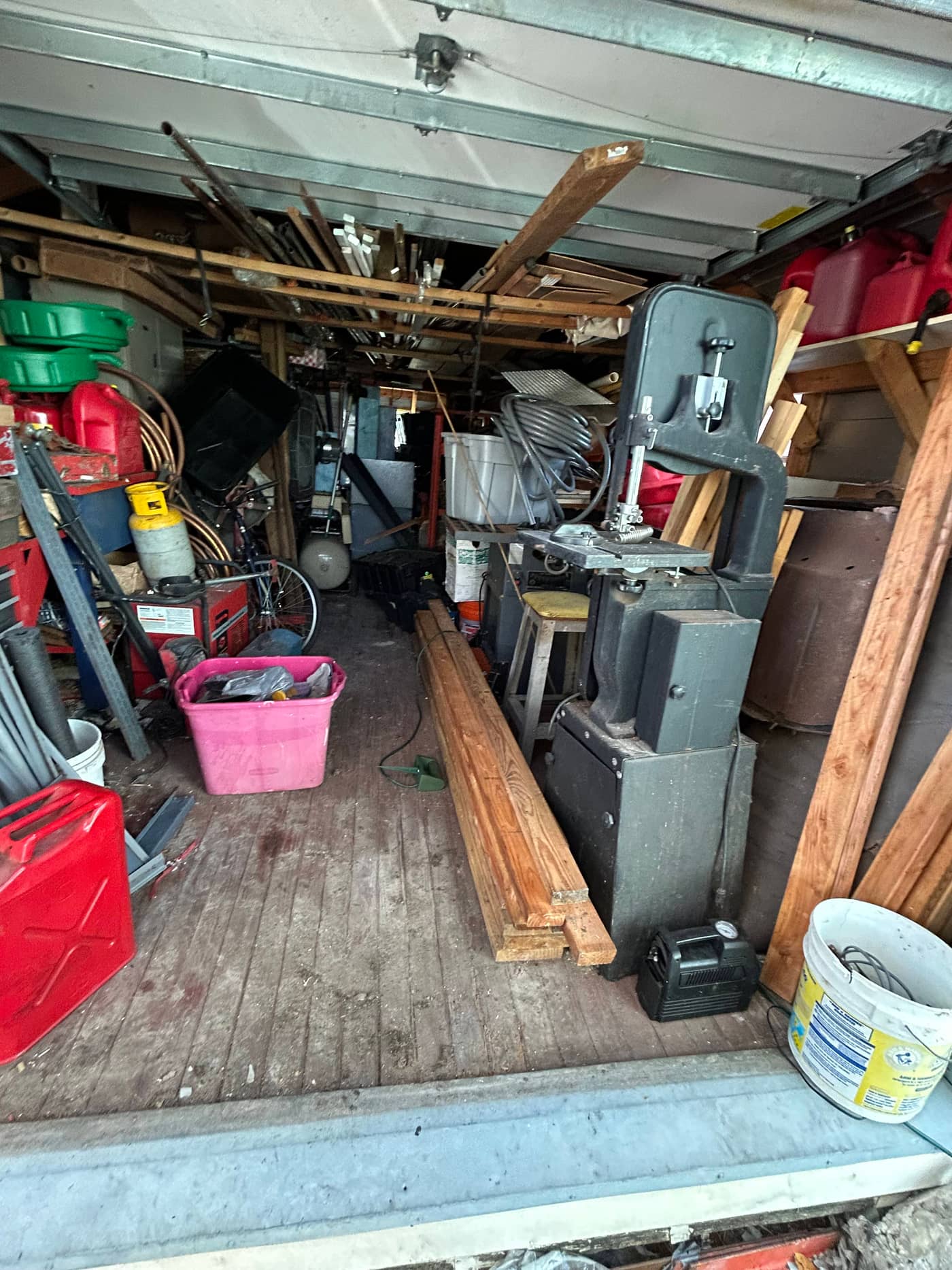 A backyard shed packed floor to roof with offcuts of timber, machinery, fuel cans, buckets and plastic bins, with no floor visible