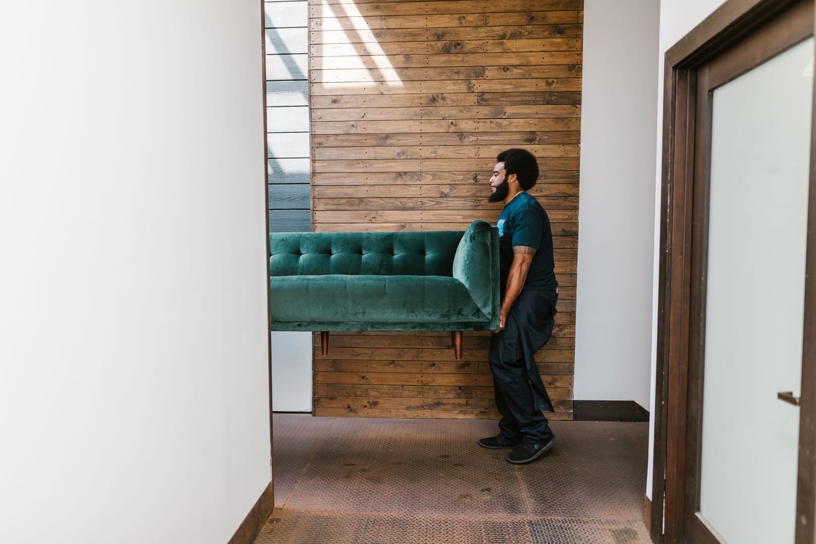 A mover carrying a green sofa out through a doorway